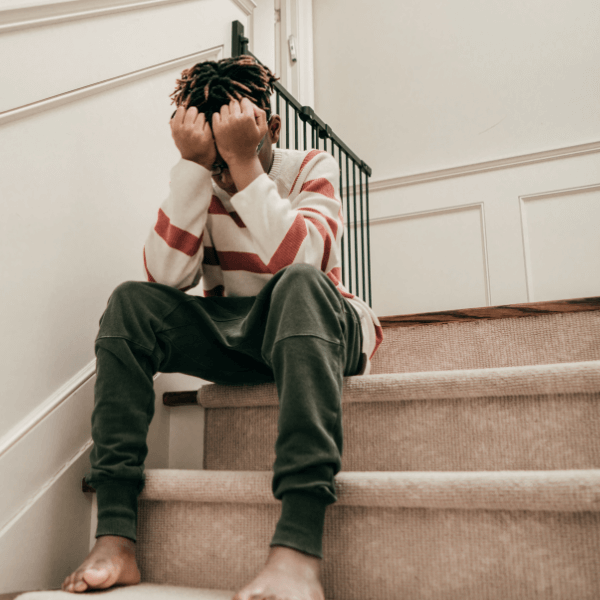 African American teen boy sitting on carpeted steps at home in distress