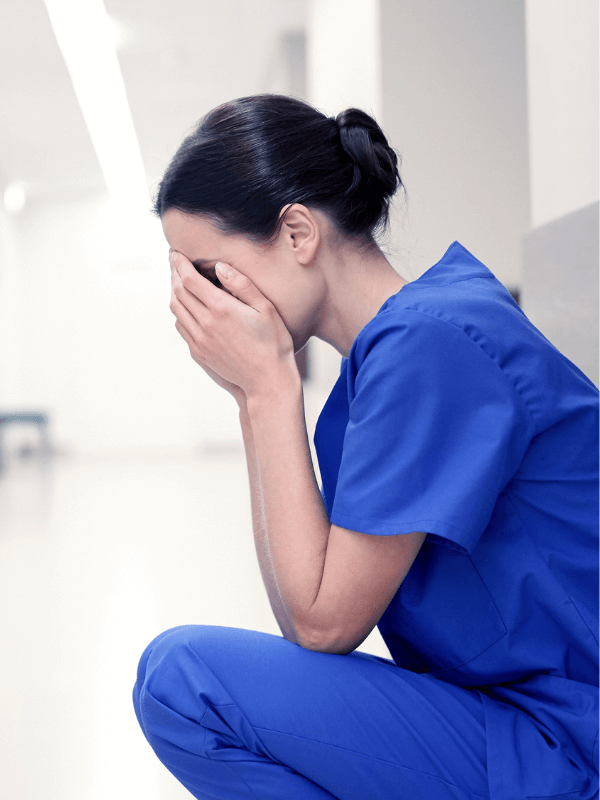 Young female healthcare worker squatting down with her hands covering her face