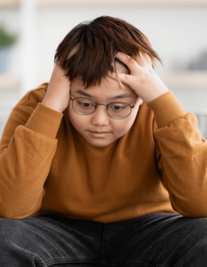 Young Asian teen sitting with his hands on his head looking frustrated