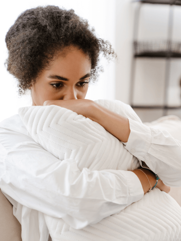 Young black woman looking sad and holding a pillow that partially covers her face