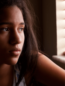 Adolescent black girl with a concerned expression looking out of the window