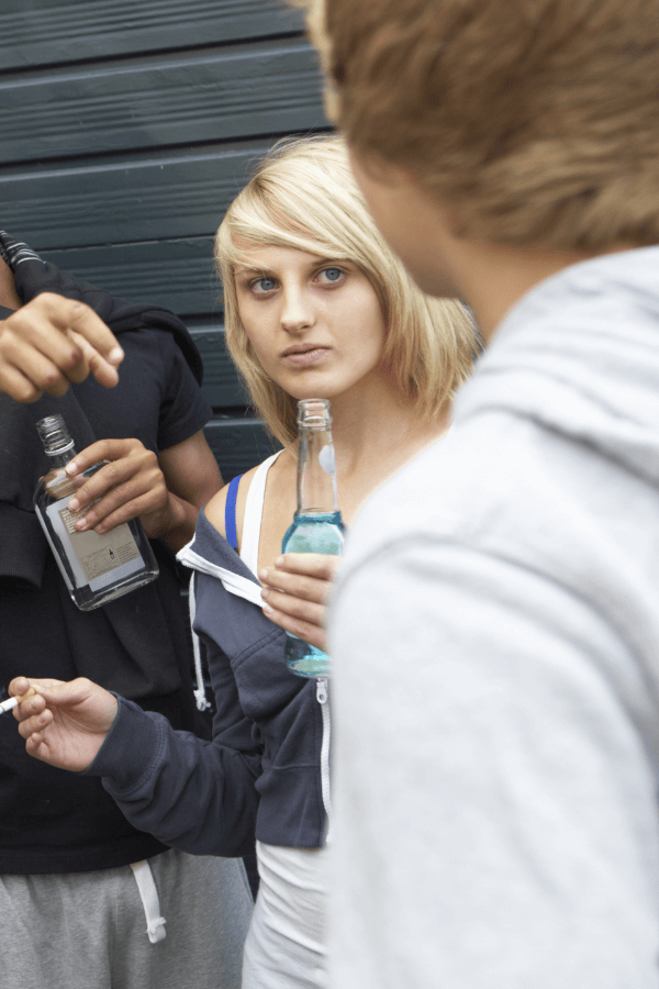 Teenage girl outdoors drinking and smoking with other kids