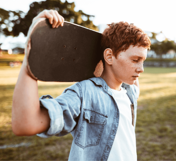Adolescent boy walking with his eyes closed and his skateboard across the back of his shoulders