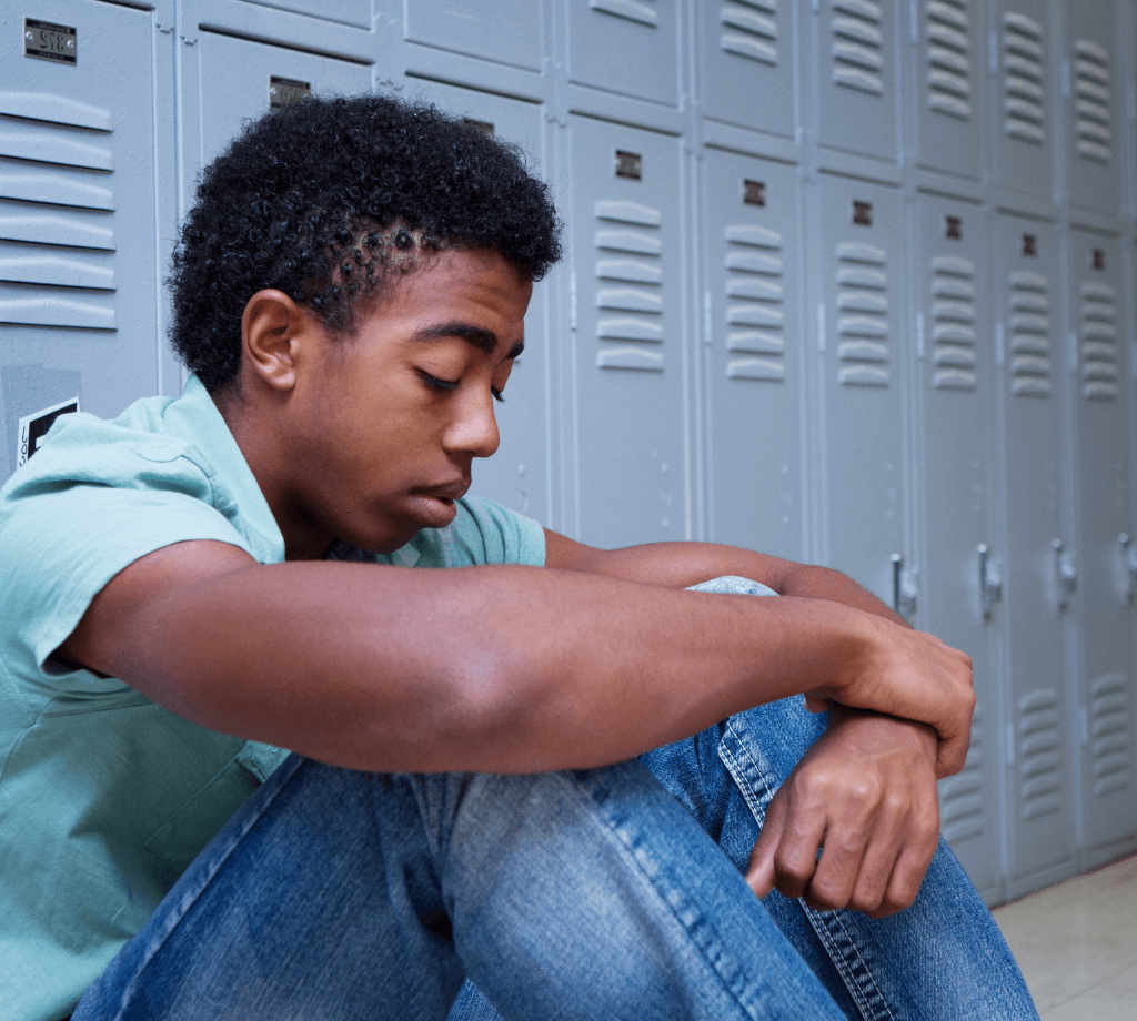 African American adolescent boy sitting in front of school lockers with his head down