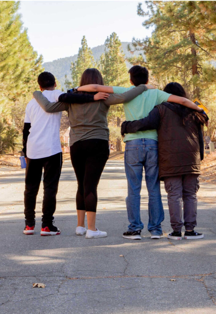four teens hugging each other in the woods