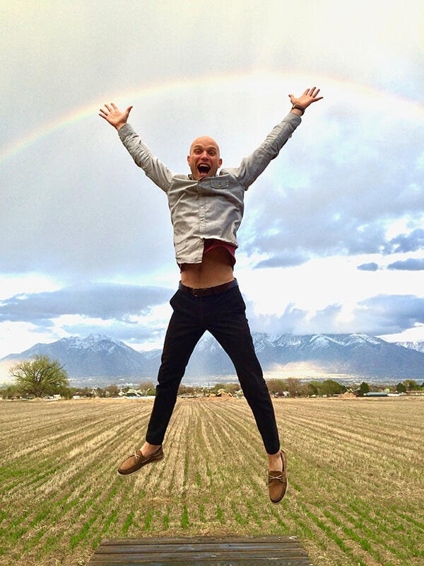 man jumping for joy in a field under a rainbow