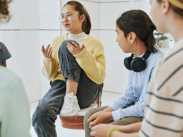 An adolescent girl talks during group therapy as other kids listen