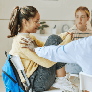 An adolescent girl in a support group, sitting with her feet on a chair, as an unseen therapist puts his hand on her shoulder.