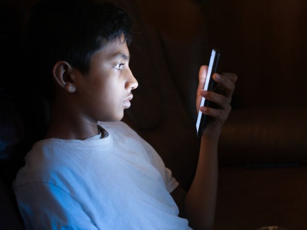 A young teen holds his mobile phone at night and stares at the screen