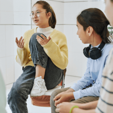 An adolescent girl talks during group therapy as other kids listen