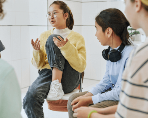 An adolescent girl talks during group therapy as other kids listen
