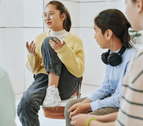 An adolescent girl talks during group therapy as other kids listen