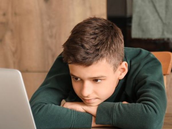 Adolescent boy sitting in the kitchen using a laptop for online therapy