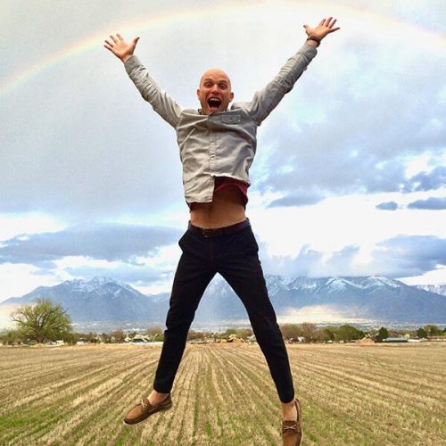 man jumping for joy in a field under a rainbow