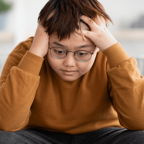 Young Asian teen sitting with his hands on his head looking frustrated