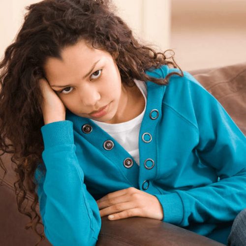 young girl sits on the couch struggling with mental health issues