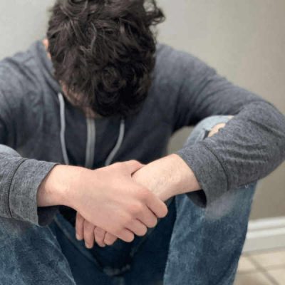 Teenage boy sitting on the floor against a wall with his head down