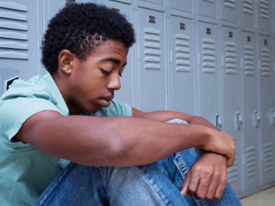 African American adolescent boy sitting in front of school lockers with his head down