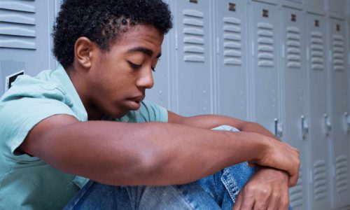 African American adolescent boy sitting in front of school lockers with his head down