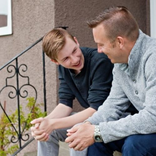 A father and son sitting on the steps outside their house while talking