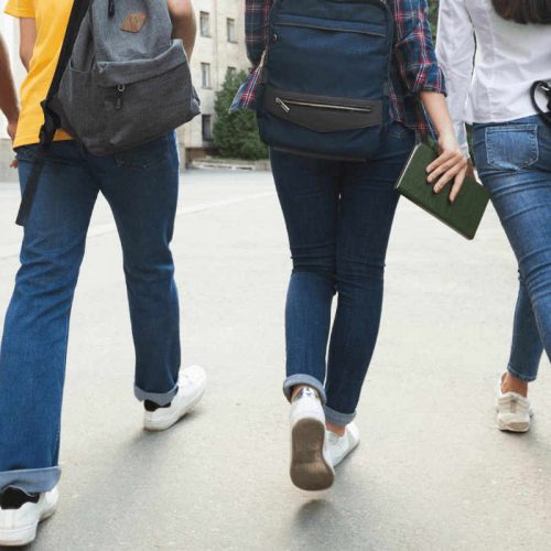 Shoulder-to-feet view of teenagers with backpacks walking