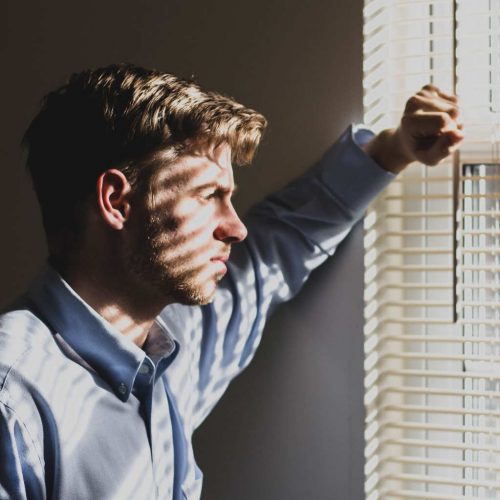 young man looks out of a window in a dark room as he struggles with teen traumatic disorder