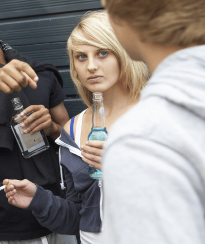 Teenage girl outdoors drinking and smoking with other kids