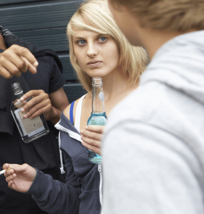 Teenage girl outdoors drinking and smoking with other kids