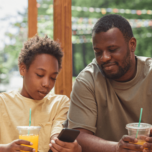 An adolescent boy using his phone for family therapy as his father looks on