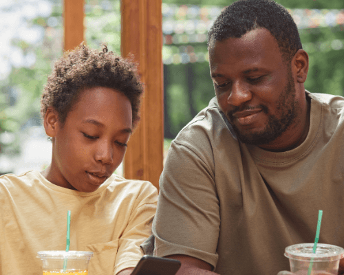 An adolescent boy using his phone for family therapy as his father looks on