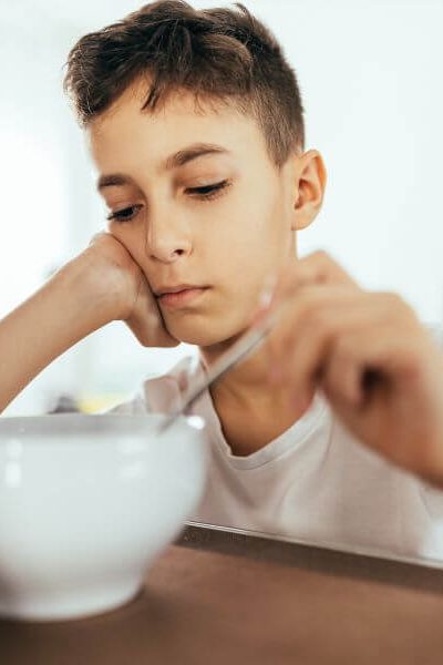 Adolescent boy sitting at a table to eat, but he has no appetite