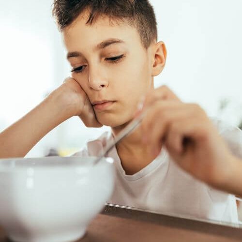 Adolescent boy sitting at a table to eat, but he has no appetite