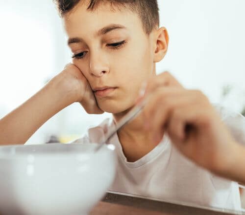 Adolescent boy sitting at a table to eat, but he has no appetite