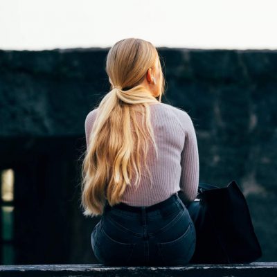 Young teen girl sits with back turned struggling with mental health issues.