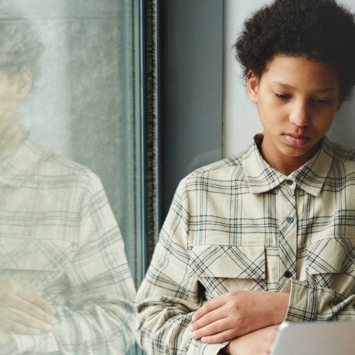 Sad adolescent sitting near a window during online therapy