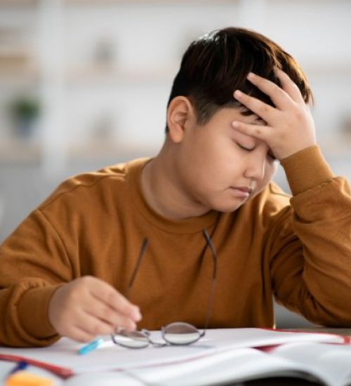 An adolescent boy is exhausted as he sits at a table trying to do homework