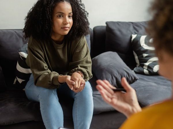 A teen girl sitting on a couch, listening to her mental health counselor