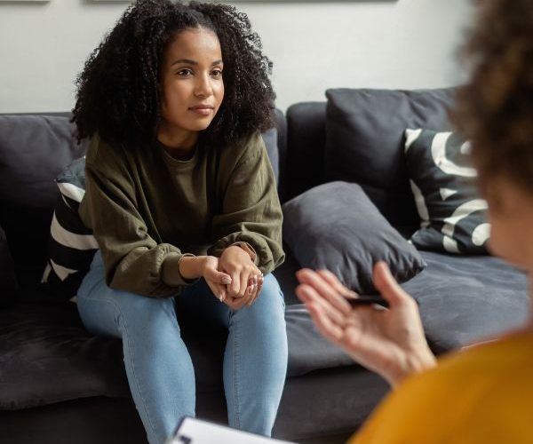 A teen girl sitting on a couch, listening to her mental health counselor