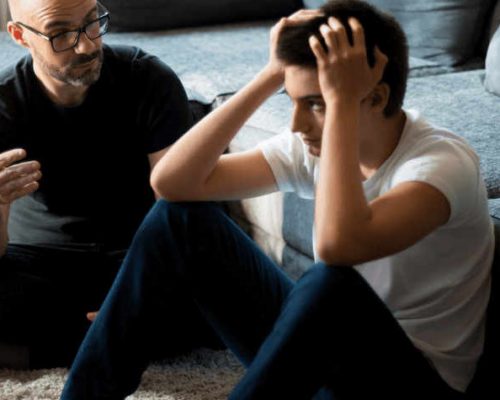 young teen boy sitting on the floor with a mental health professional