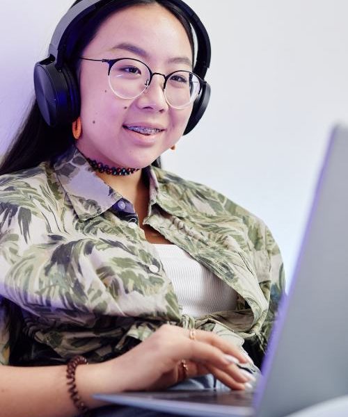 A teen girl uses a laptop and wears headphones during web-based mental health therapy